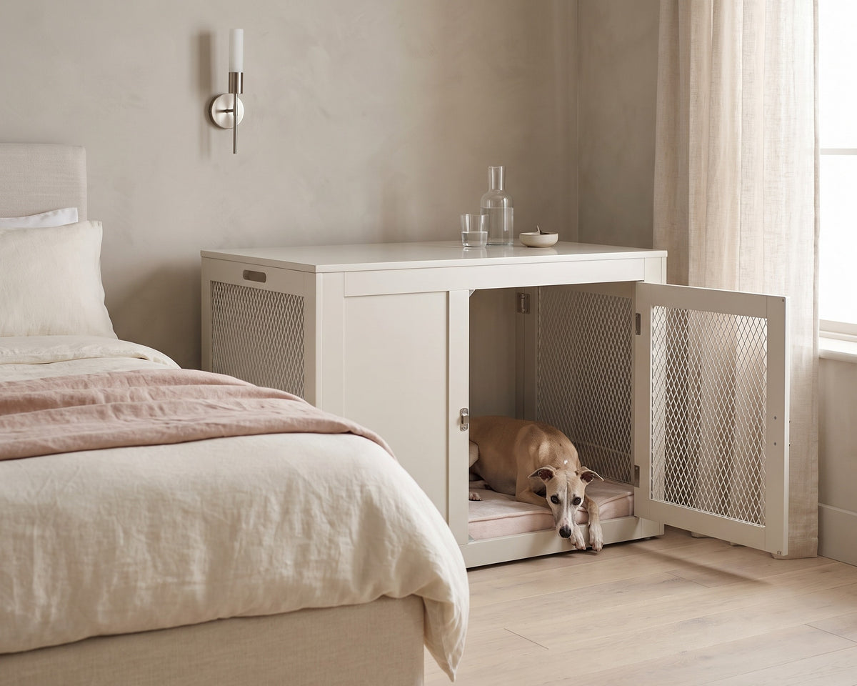 A Whippet lying at the open front door of a Fresco Dog Crate in Lunar beside the bed in a calm bedroom